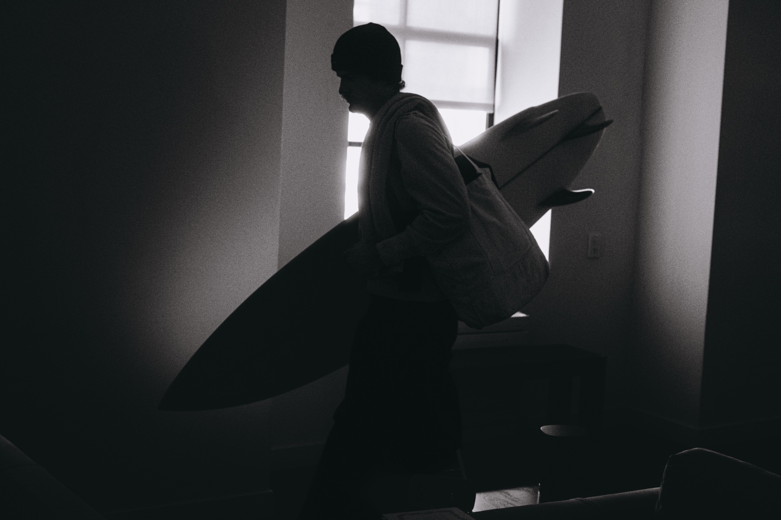 Silhouetted surfer carrying a board indoors